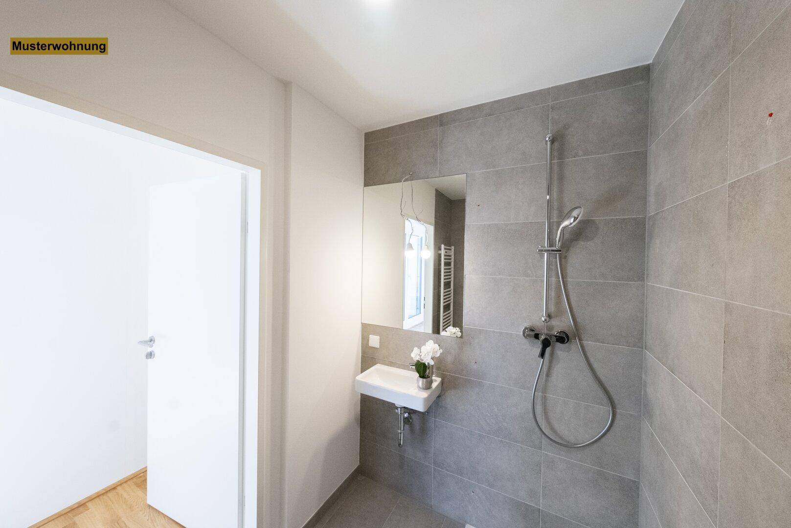 Modernes Badezimmer mit grauen Fliesen, wandhängendem Waschbecken und einer Duschkabine.
