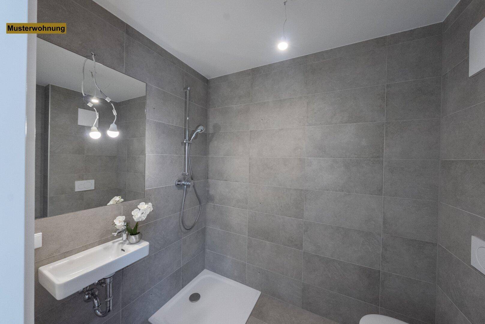 Zeitgemäßes Badezimmer mit großformatigen grauen Fliesen, Duschbereich und minimalistischem Waschbecken.