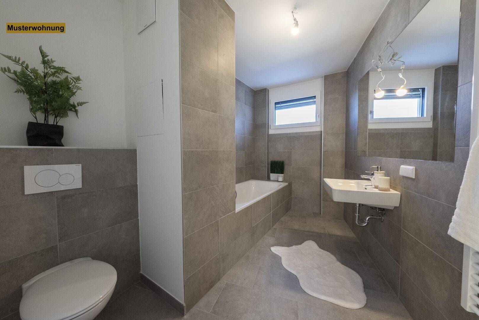 Modernes Badezimmer mit grauen Fliesen, Badewanne, wandhängendem WC und Fenster für Tageslicht.
