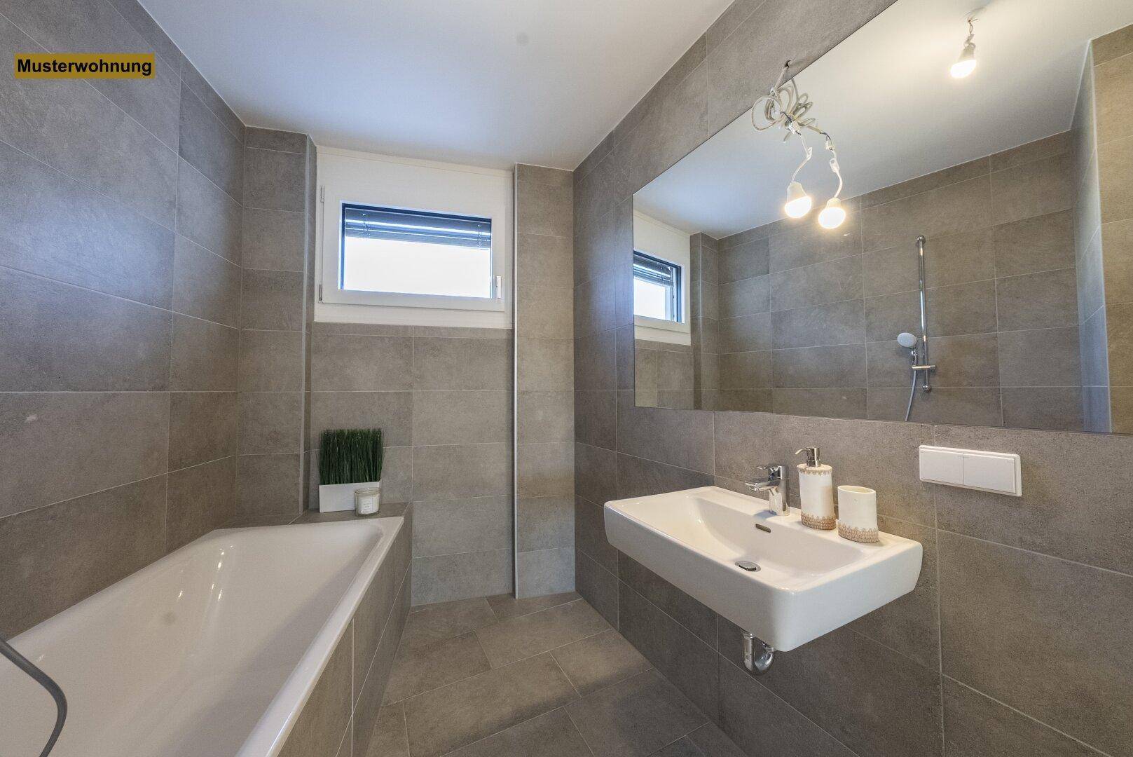 Helles Badezimmer mit Badewanne, modernem Waschbecken und Fenster, komplett gefliest in Grau.