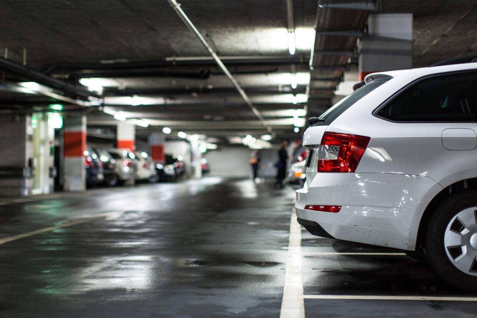 Nasse Fahrbahn in einer Tiefgarage mit geparkten Autos und sichtbaren Beleuchtungselementen.