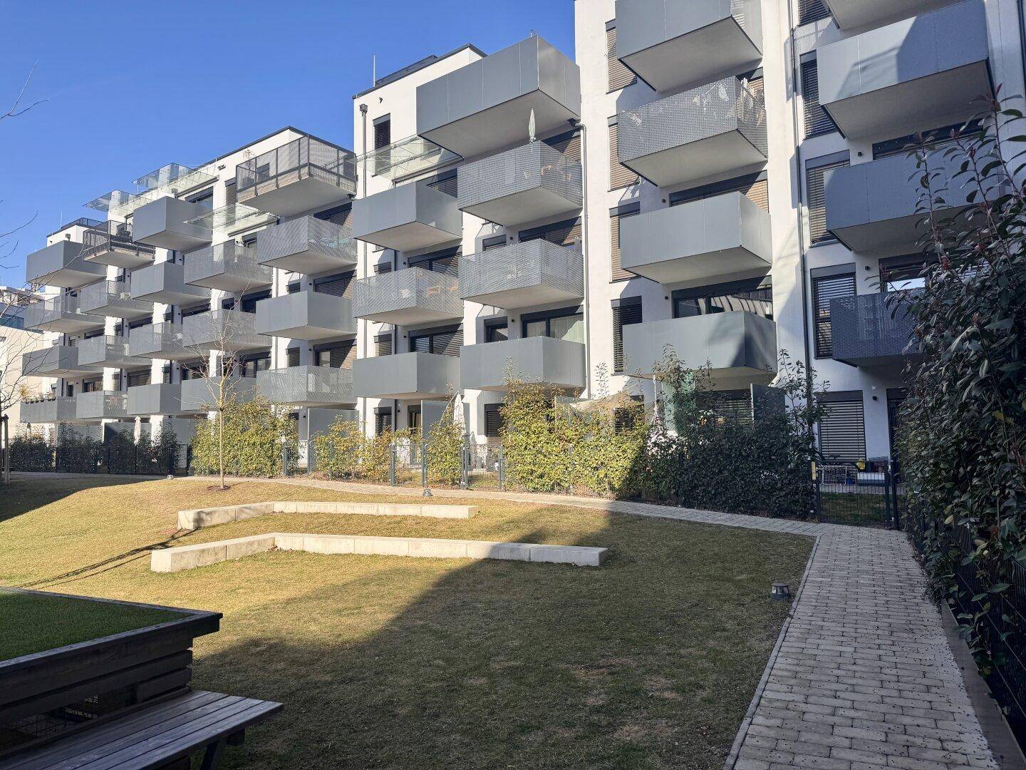 Weitläufige Außenansicht einer modernen Wohnanlage mit Balkonen und Gemeinschaftsgarten bei Sonnenschein.