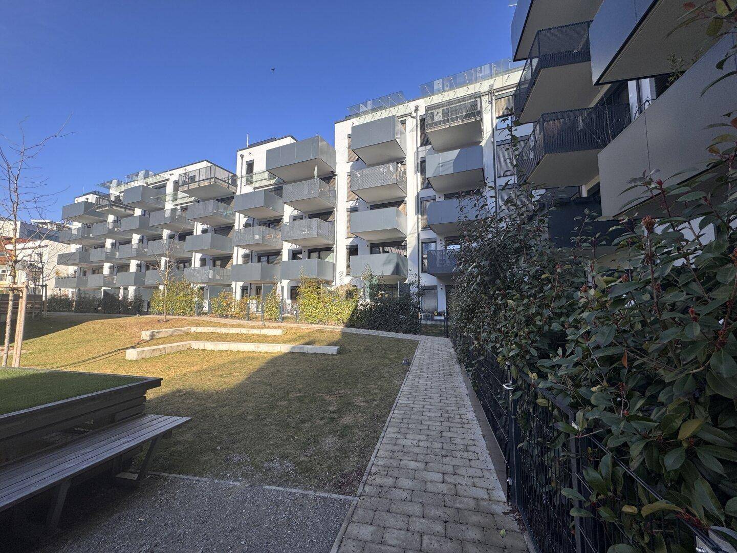 Ansicht der modernen Wohngebäude mit zahlreichen Balkonen und einem grünen Innenhof unter klarem Himmel.