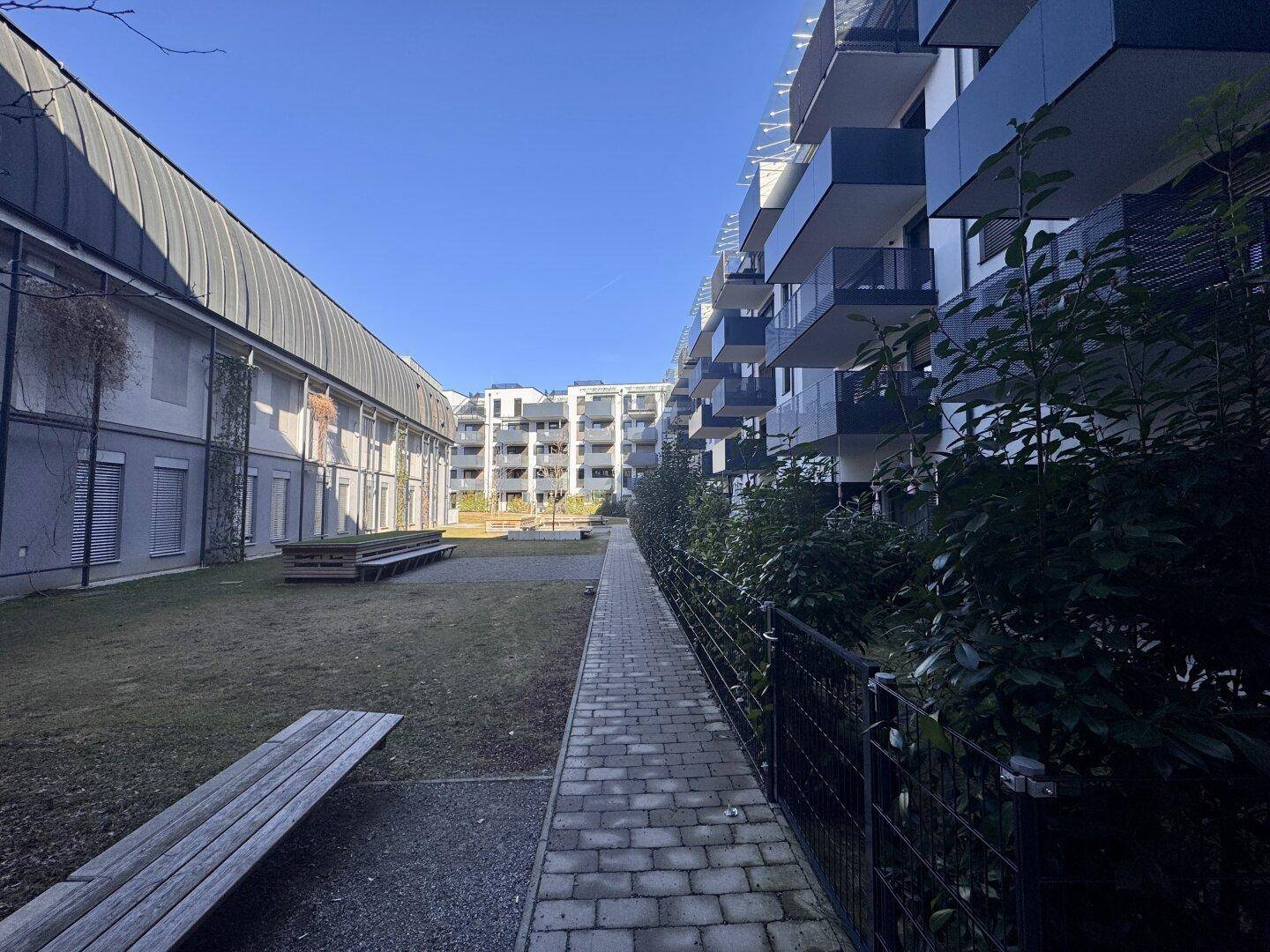 Blick in den grünen Innenhof zwischen zwei modernen Wohngebäuden mit Sitzbänken und Wegen.