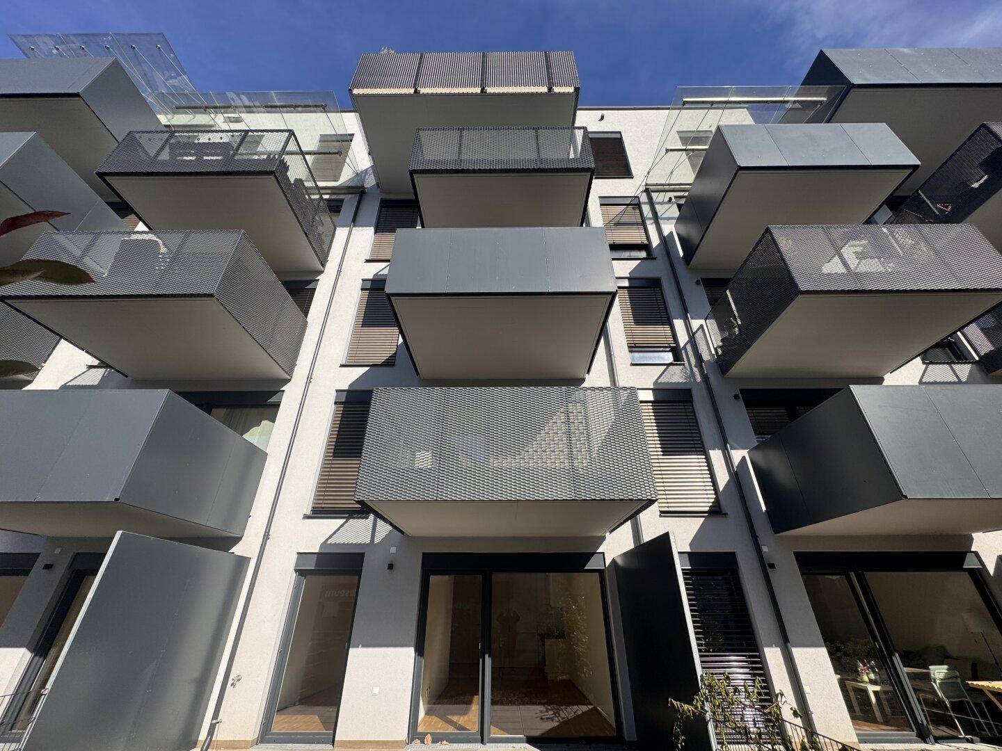 Nahaufnahme der modernen Fassade mit gestaffelten Balkonen und großen Fenstern bei hellem Licht.