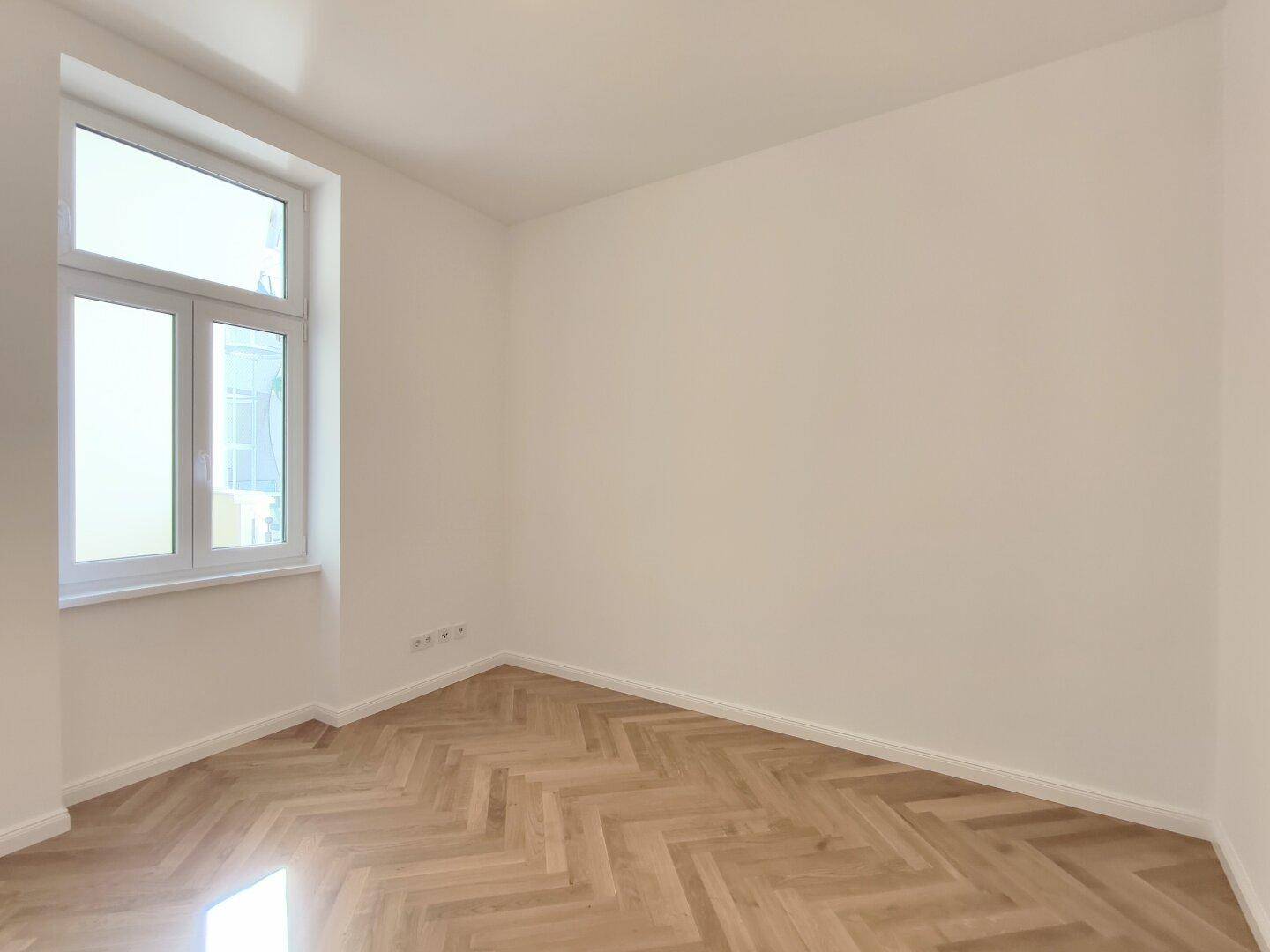 Ruhiges Schlafzimmer mit Fischgrätparkett und einem großen Fenster, ideal für erholsame Nächte.