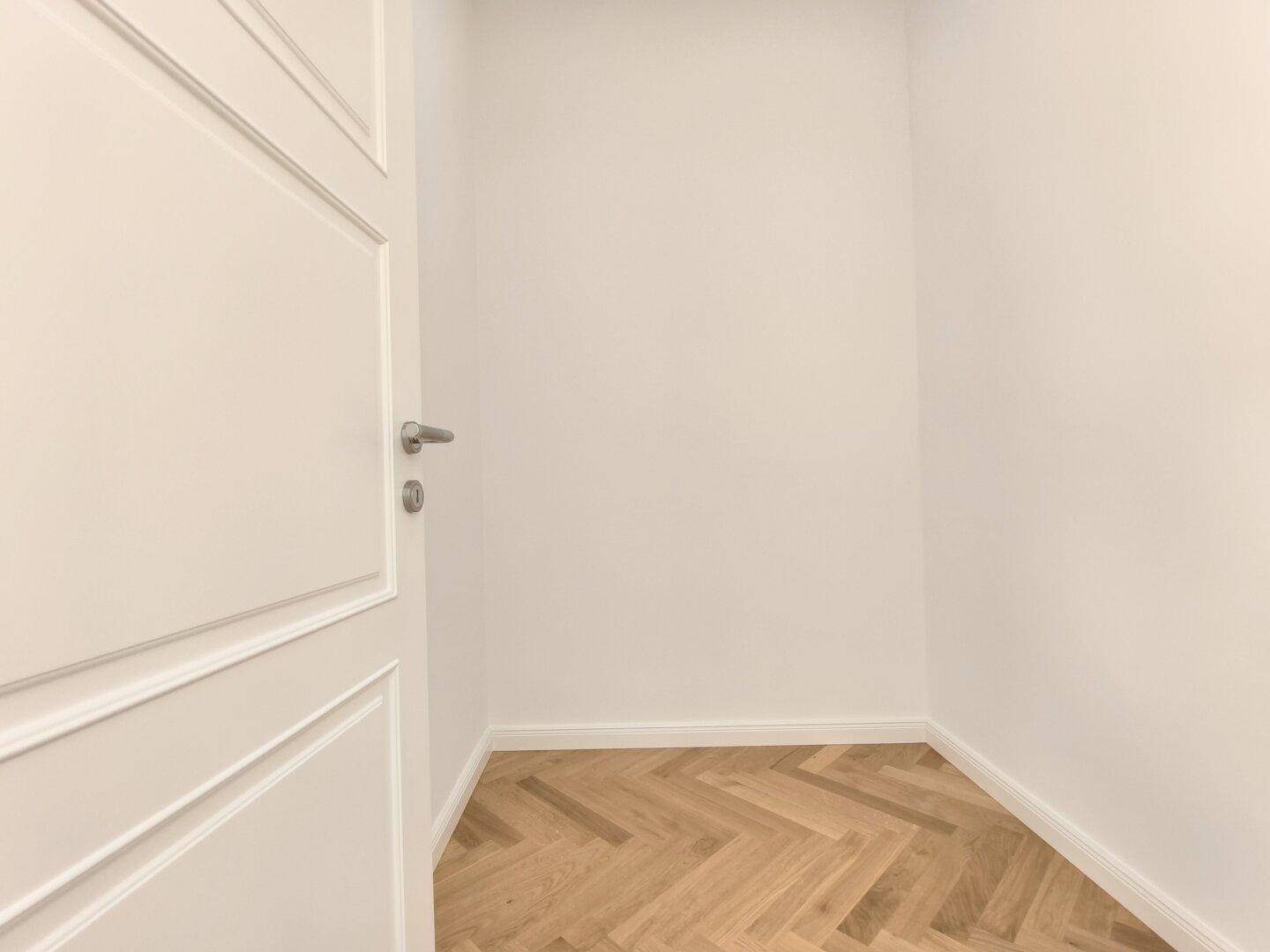 Praktischer Abstellraum mit Fischgrätparkett und weiß gestrichenen Wänden, ideal für zusätzlichen Stauraum.