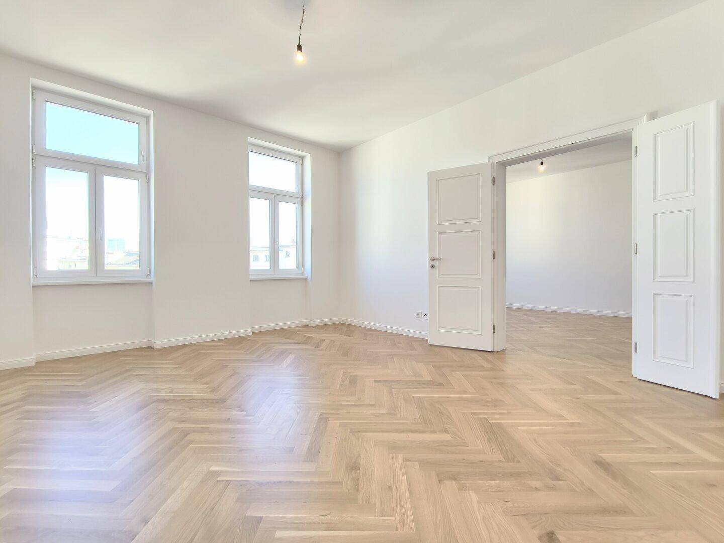Geräumiges, helles Zimmer mit Fischgrätparkett und hohen Fenstern, bereit zur individuellen Gestaltung.
