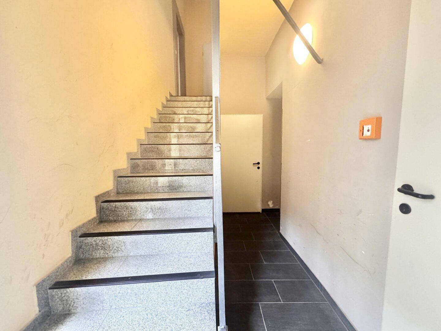 Treppenhaus mit Steinstufen und Flur mit dunklen Fliesen, führt zu weiteren Wohnbereichen.