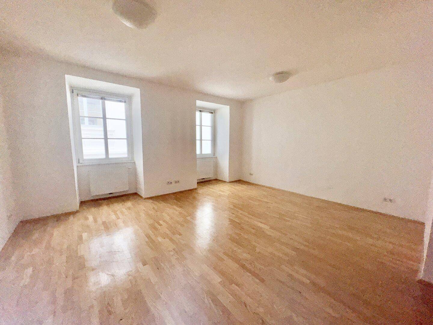 Geräumiges Zimmer mit hellem Parkettboden und zwei großen Fenstern für viel Tageslicht.