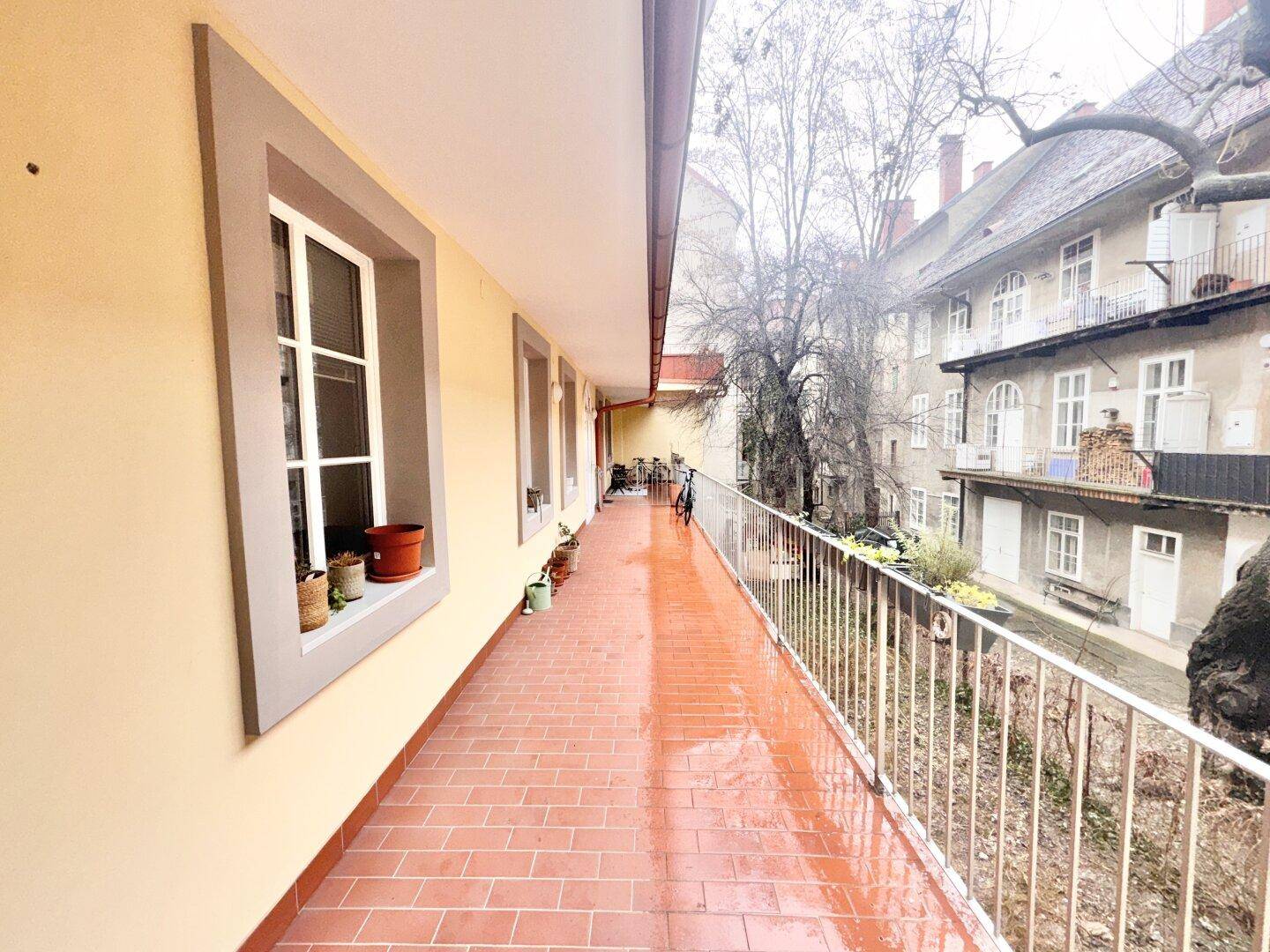 Langer Außenbalkon mit Terrakottafliesen und Blick auf den Innenhof des Gebäudes.