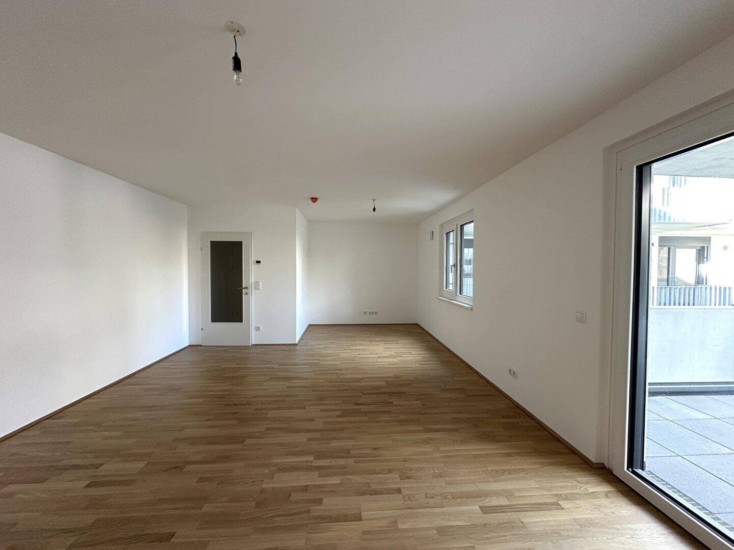 Geräumiger Wohnbereich mit hellem Parkettboden und Zugang zu einem großen Balkon.