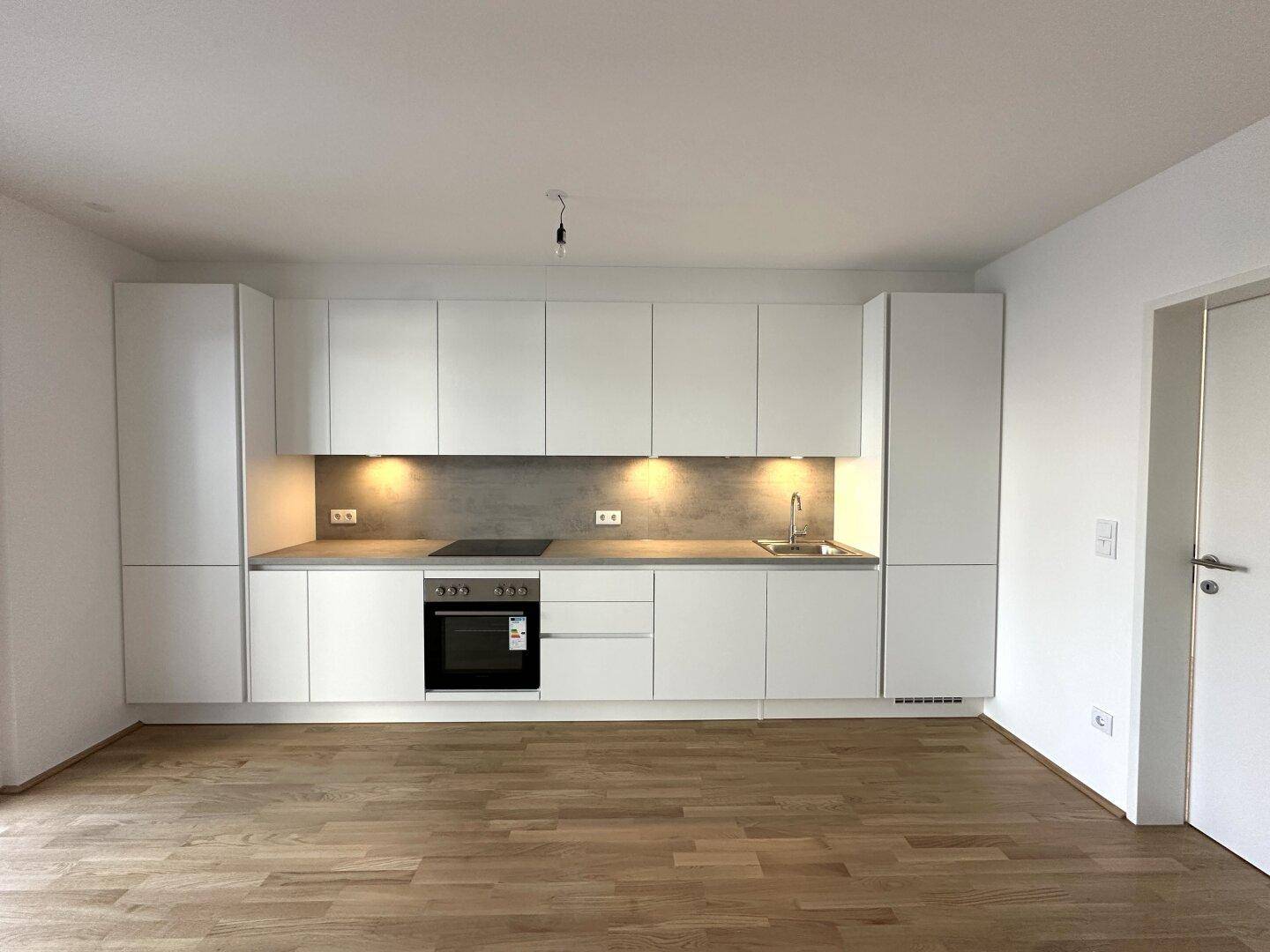 Moderne Einbauküche in Weiß mit integrierten Geräten und heller Arbeitsplatte.
