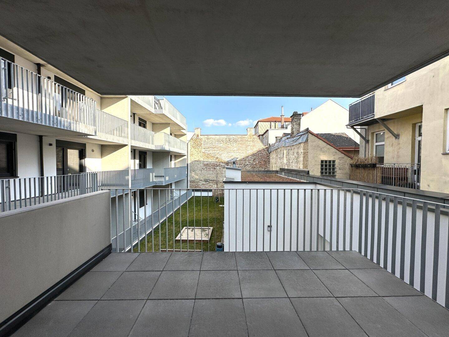 Geräumiger Balkon mit Fliesenboden und Blick auf den begrünten Innenhof.