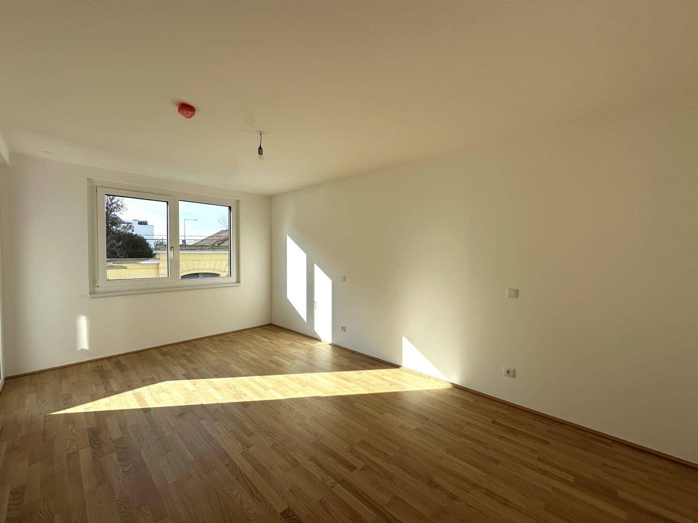 Sonniges Schlafzimmer mit Parkettboden und großem Fenster, das viel Licht hereinlässt.