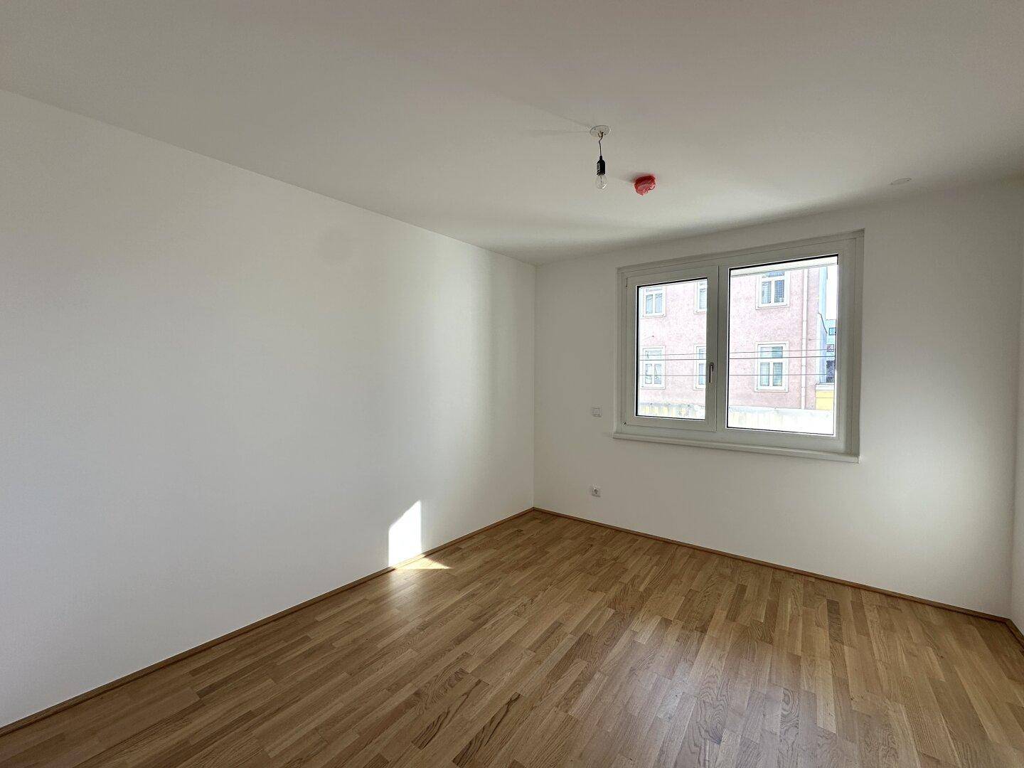 Ruhiges Schlafzimmer mit hellem Parkettboden und Fenster mit Blick ins Grüne.