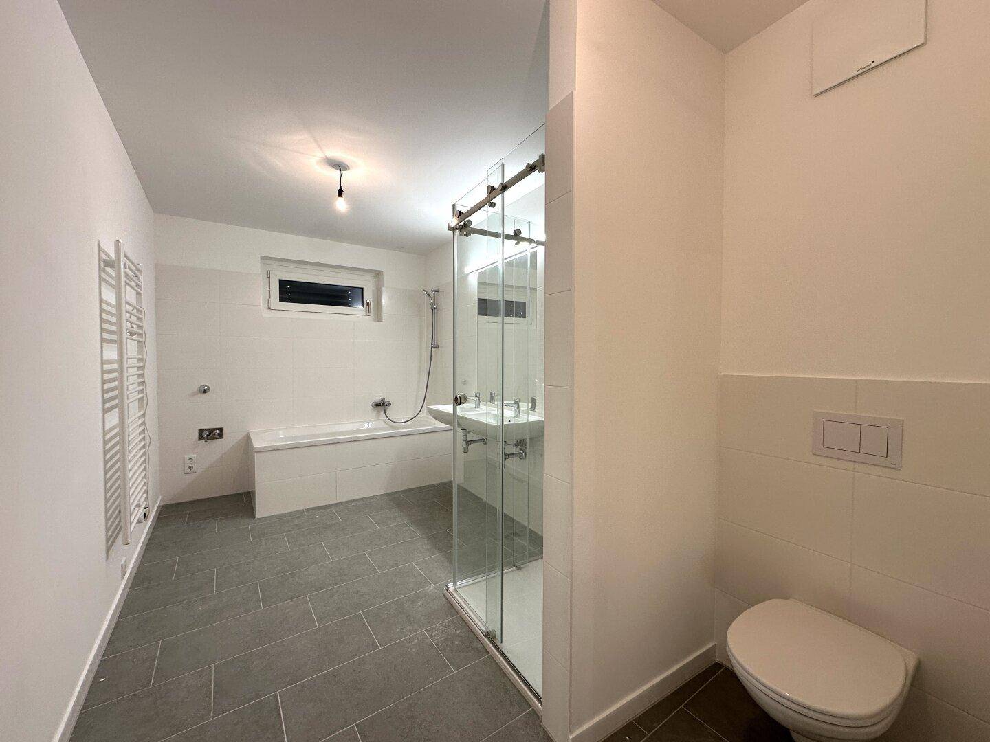 Modernes Badezimmer mit Badewanne, Dusche, WC und beheiztem Handtuchhalter.