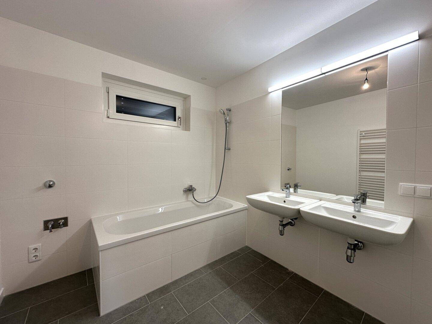 Helles Badezimmer mit Badewanne, Doppelwaschbecken und großem Spiegel mit Beleuchtung.