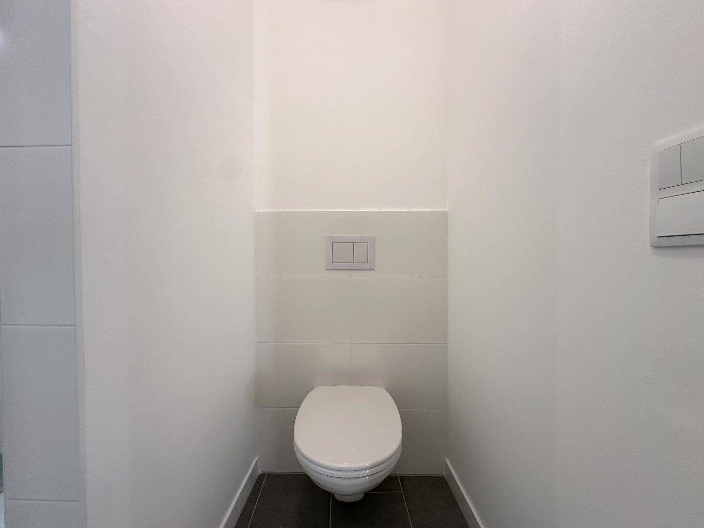 Separates WC mit wandhängender Toilette und modernen Fliesen an den Wänden.