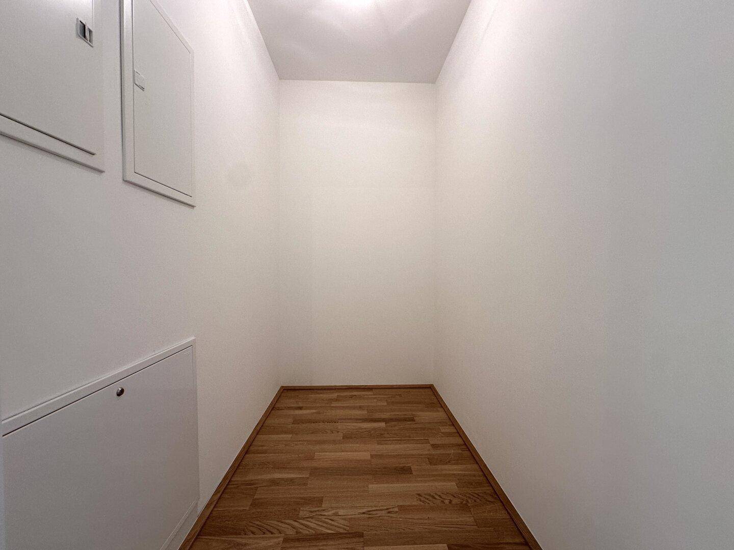 Praktischer Abstellraum mit hellem Parkettboden und Zugangsklappen in der Wand.