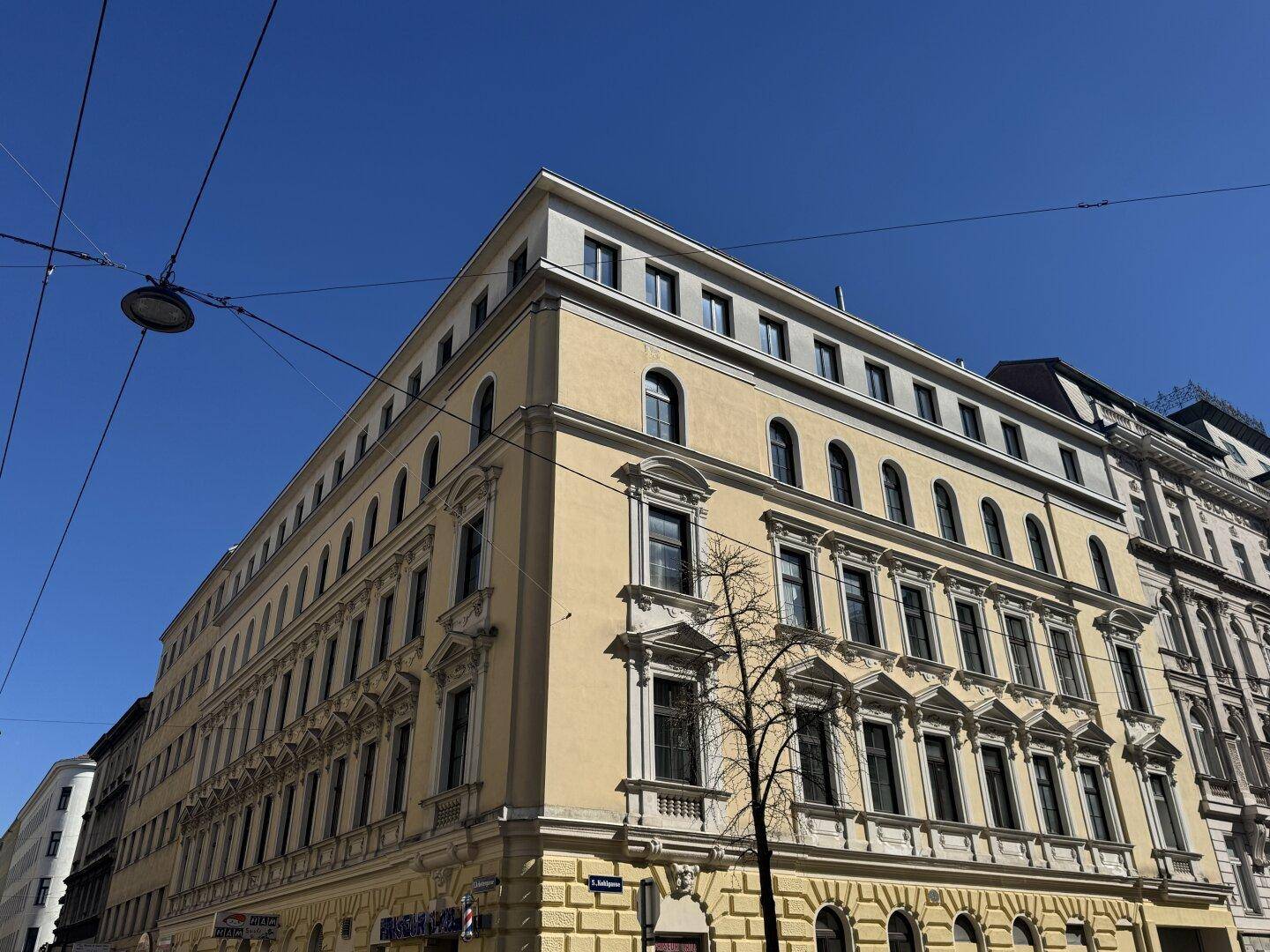 Eindrucksvolles Eckgebäude mit klassischer Architektur und vielen Fenstern unter strahlend blauem Himmel.