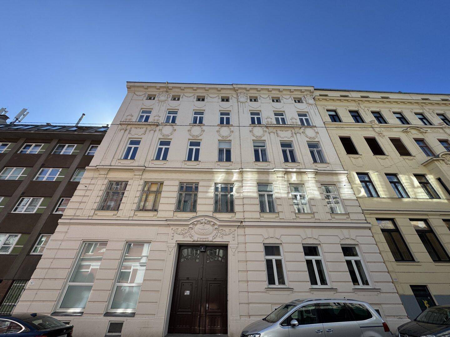 Breite Ansicht der historischen Altbaufassade mit vielen Fenstern und Verzierungen unter blauem Himmel.