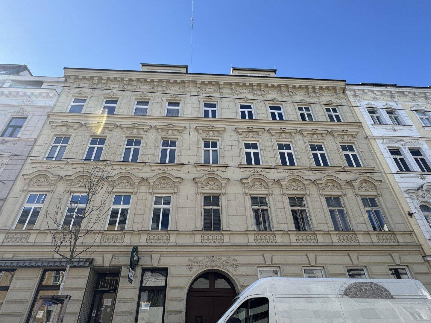 Detailansicht der historischen Fassade eines Wohnhauses mit dekorativen Elementen und blauer Himmel.