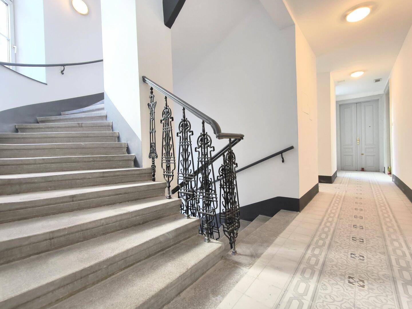 Historisches Treppenhaus mit kunstvollem Geländer und gemusterten Fliesen im Flur.