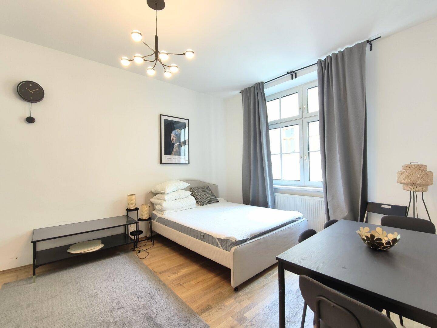 Gemütliches Studio-Apartment mit Bett, Esstisch und moderner Deckenbeleuchtung.