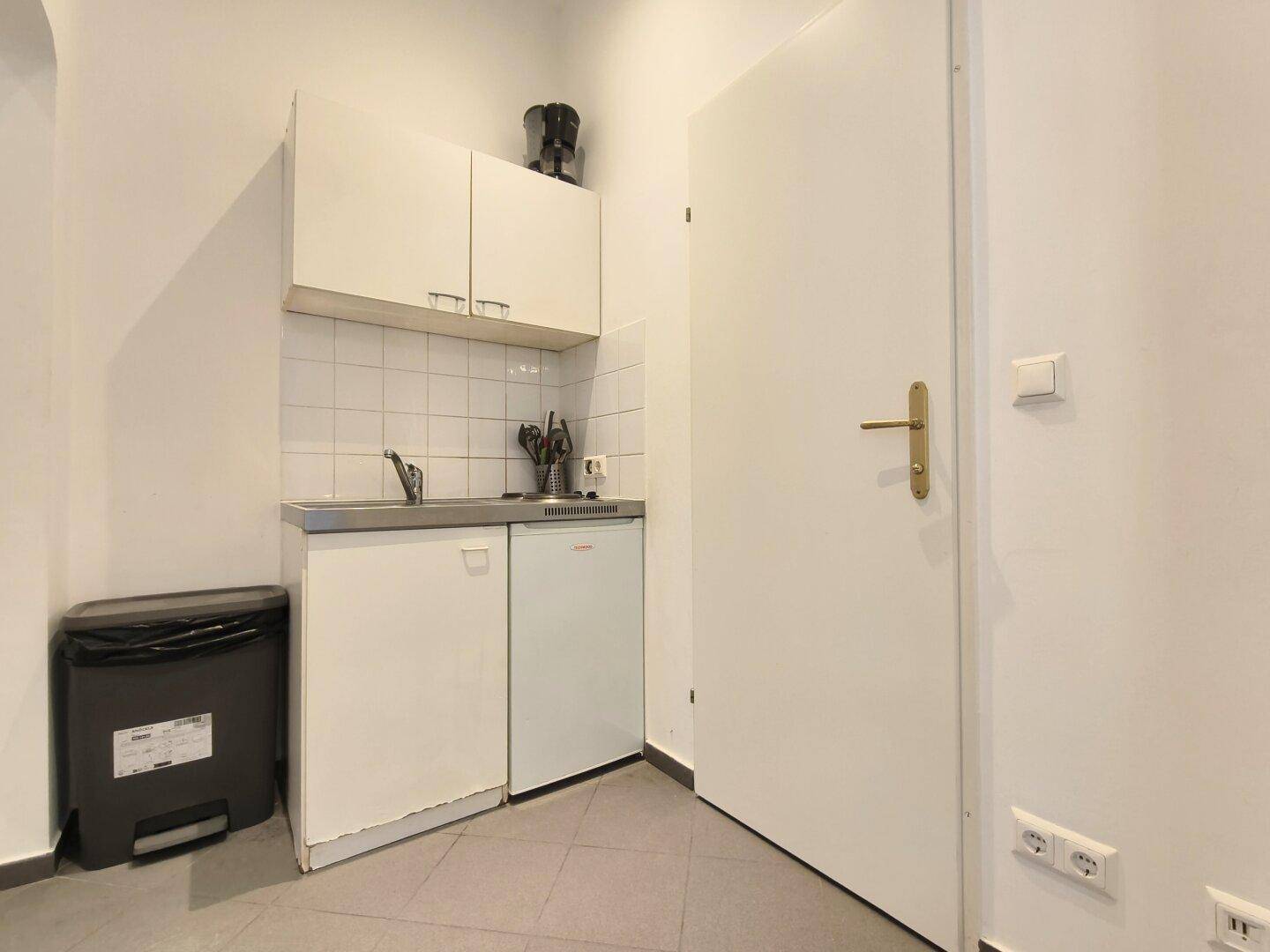 Kleine, funktionale Kochnische mit Spüle, Kühlschrank und weißen Oberschränken.