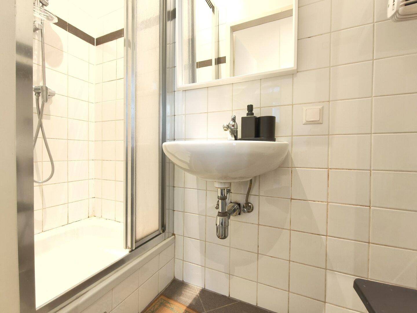 Helles Badezimmer mit Duschkabine, Waschbecken und weißen Wandfliesen.