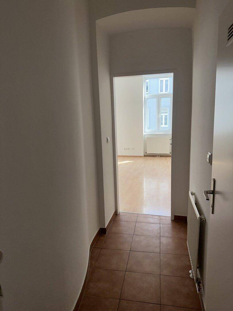 Flur mit Terrakotta-Fliesenboden, weißen Wänden und Blick in einen hellen Raum.