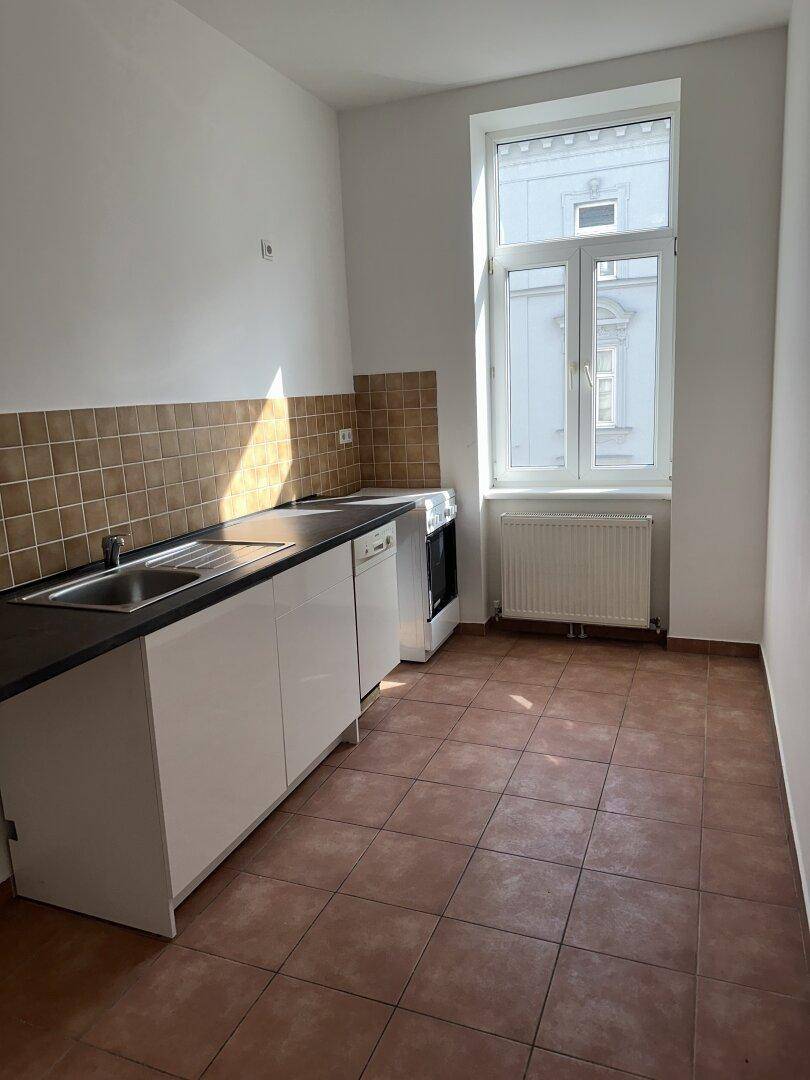 Funktionale Küche mit weißen Unterschränken, dunkler Arbeitsplatte und braunen Wandfliesen.