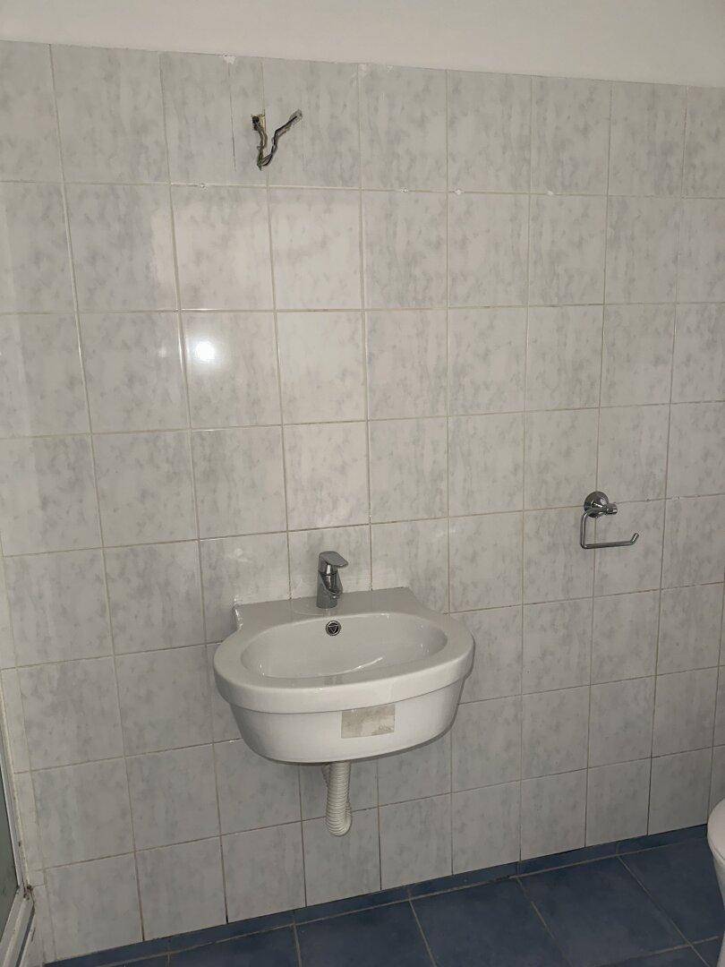Badezimmer mit weißem Waschbecken, hellblauen Fliesen an den Wänden und dunklem Boden.