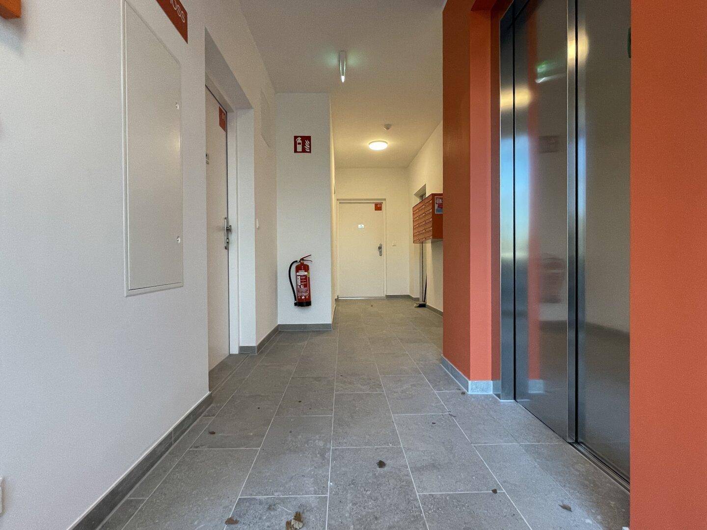 Heller Flur im Gebäude mit Zugang zum modernen Aufzug und Fliesenboden.