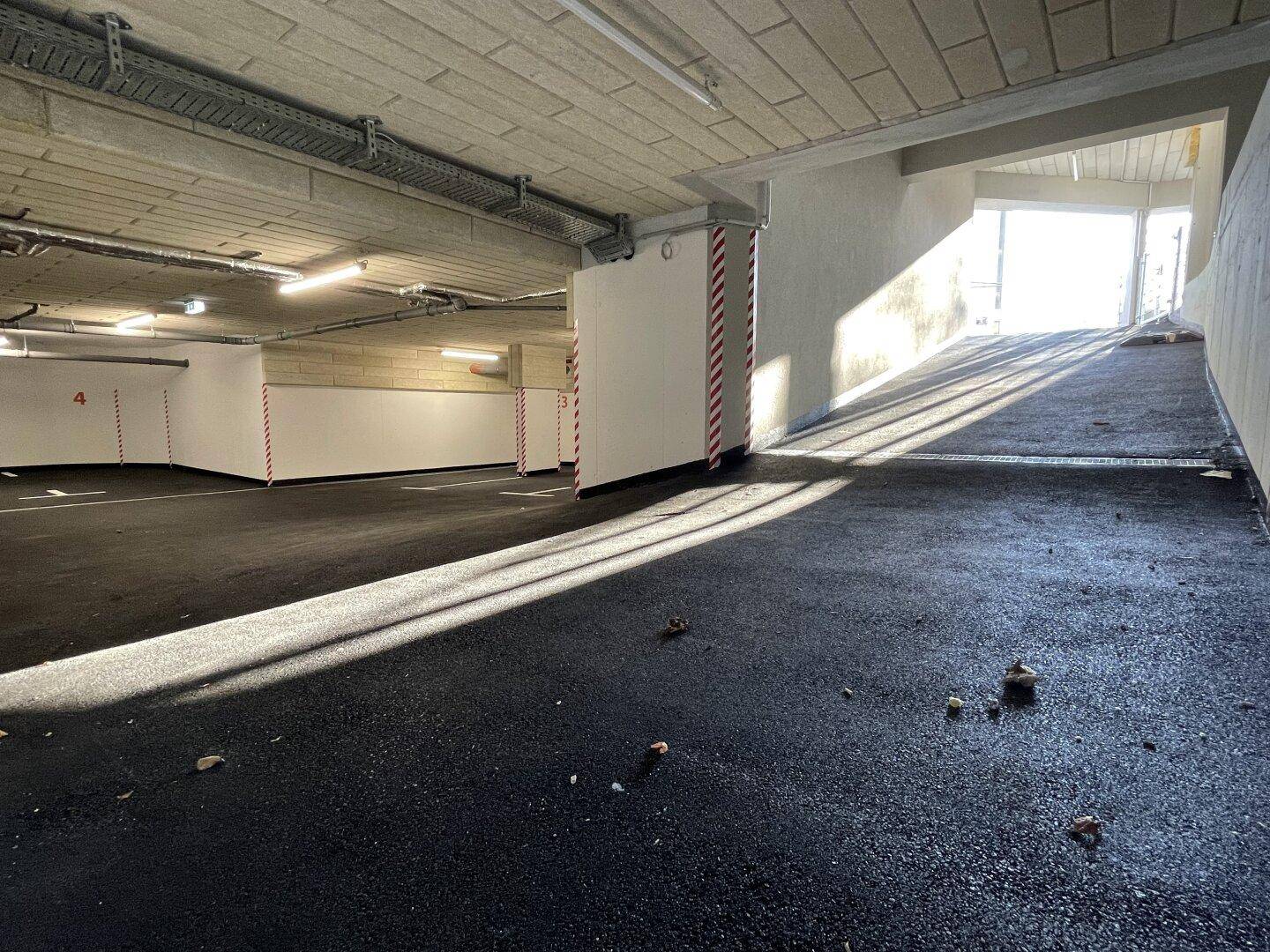 Zufahrt zur Tiefgarage mit markierten Stellplätzen und heller Beleuchtung.