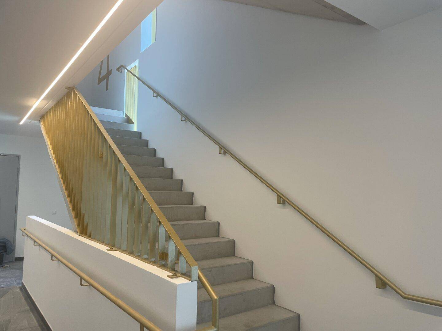 Modernes Treppenhaus mit elegantem goldenem Geländer und heller Beleuchtung, führt zu den Etagen.