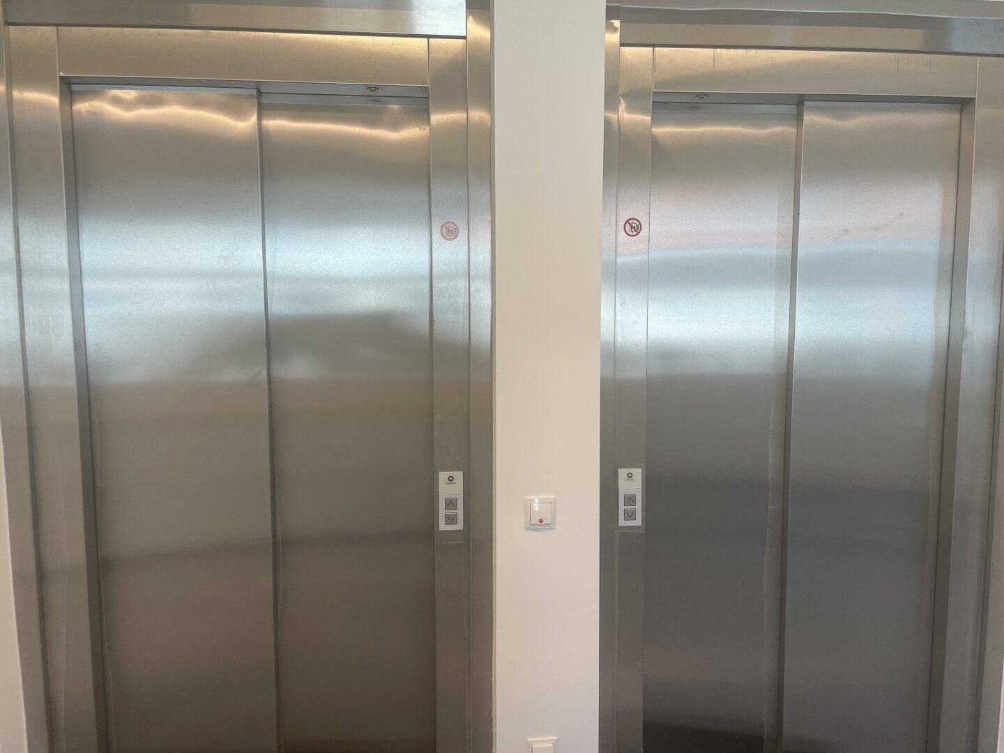 Zwei moderne Aufzüge mit Edelstahltüren in einem hellen und gepflegten Eingangsbereich.