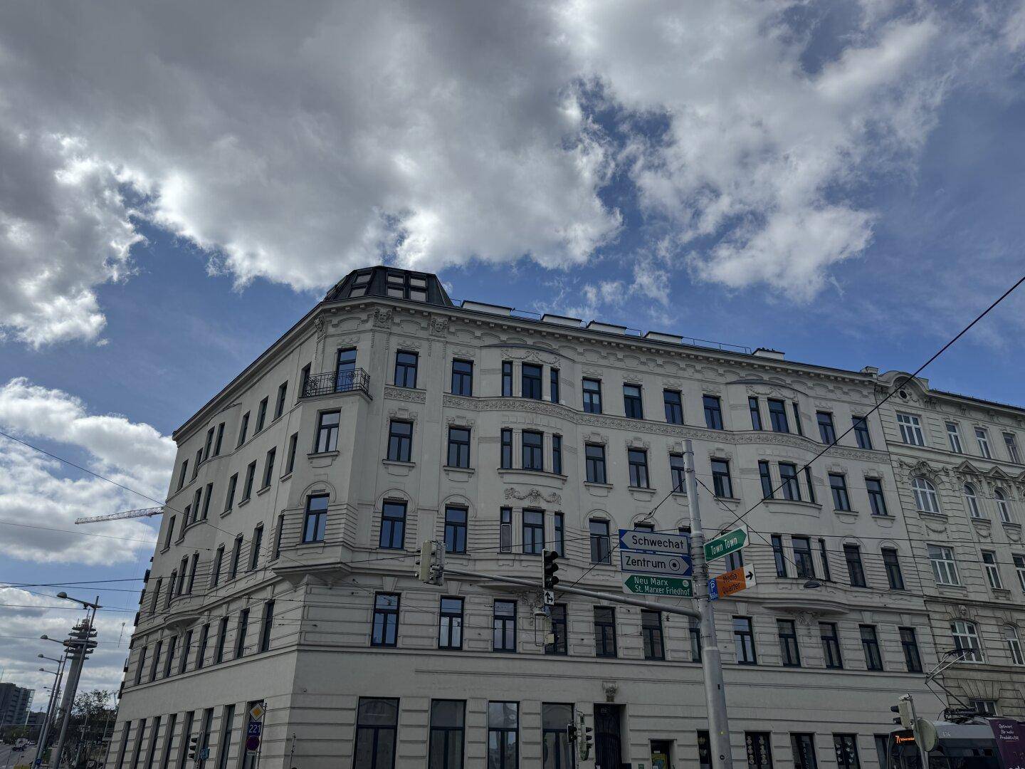 Elegantes Stadtgebäude an einer Kreuzung mit traditioneller Fassade und blauen Fenstern.