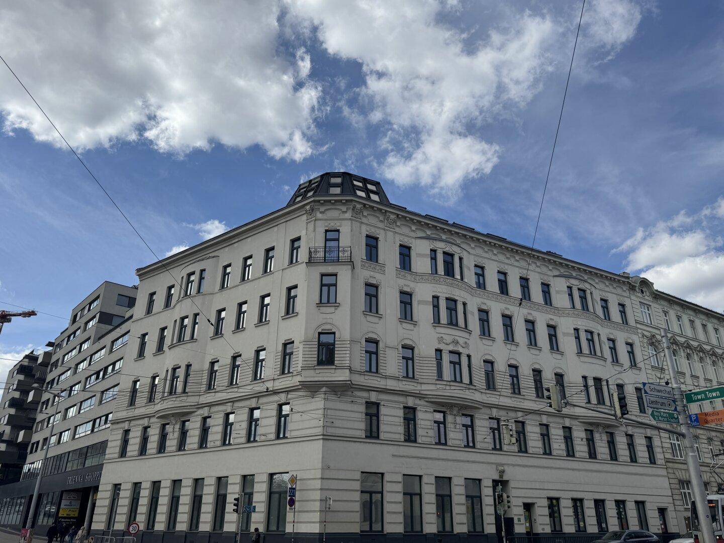 Historisches Eckgebäude mit klassischer Architektur und vielen Fenstern unter einem bewölkten Himmel.