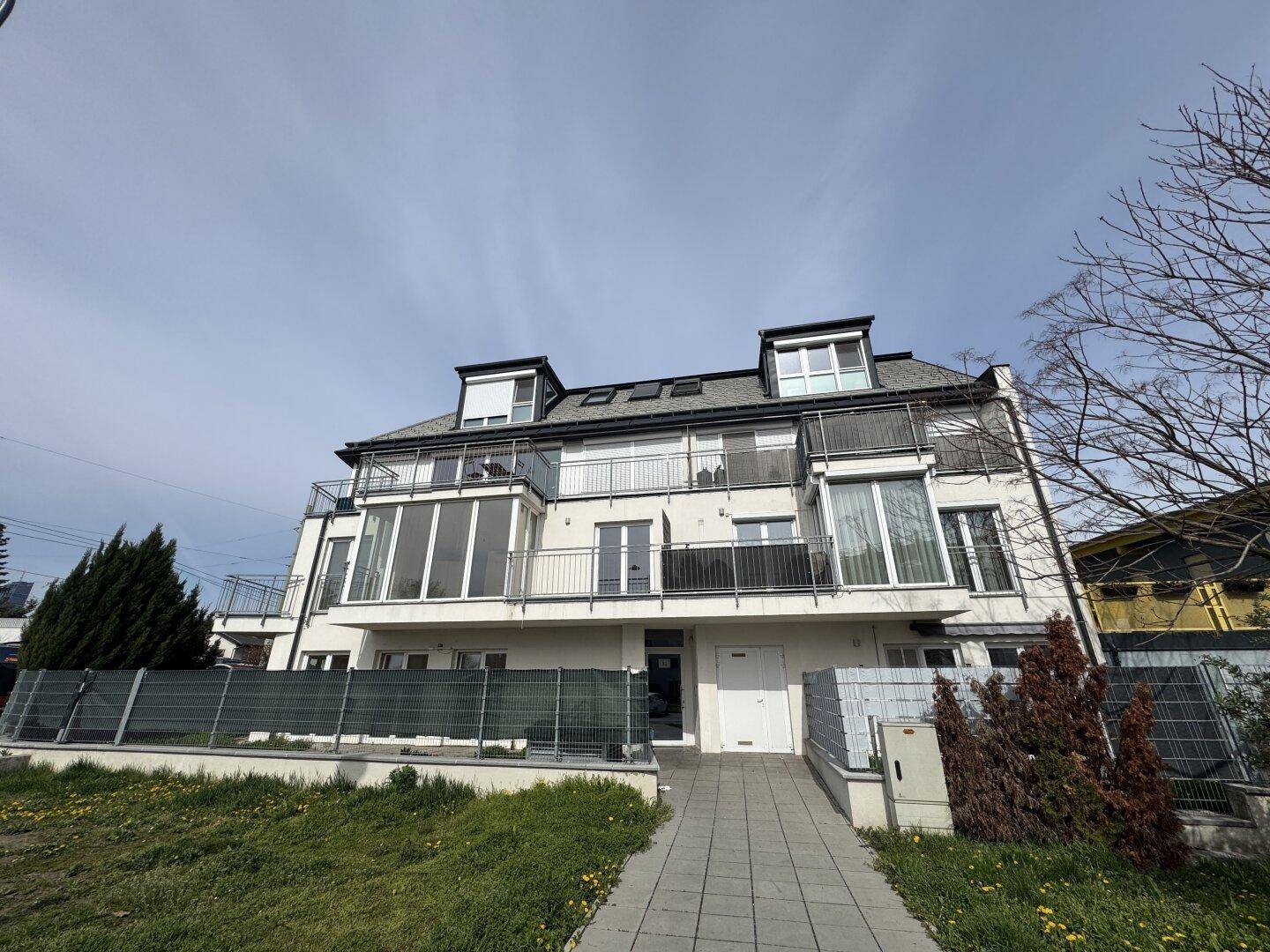 Moderne Wohnanlage mit mehreren Balkonen und großen Fensterfronten unter blauem Himmel.