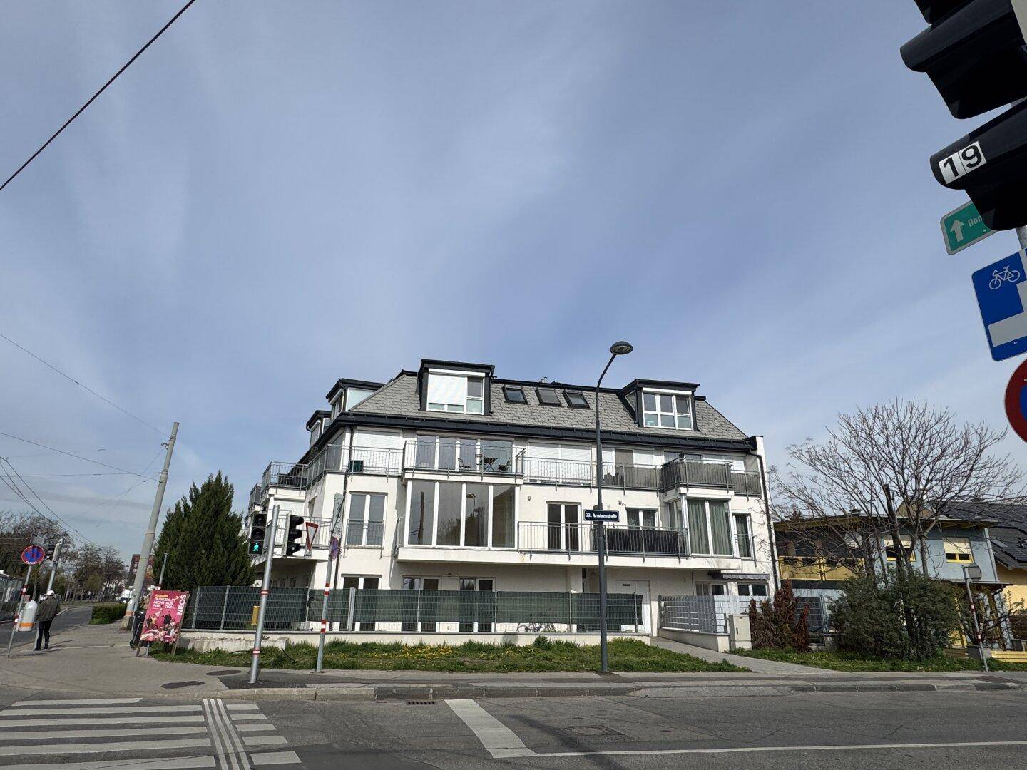 Eckgebäude einer modernen Wohnanlage mit Balkonen und großen Fenstern an einer städtischen Kreuzung.