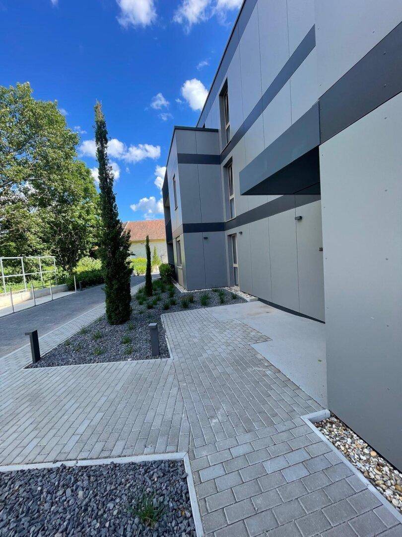 Moderne Gebäudefassade mit klaren Linien und gepflasterten Gehwegen im Außenbereich.