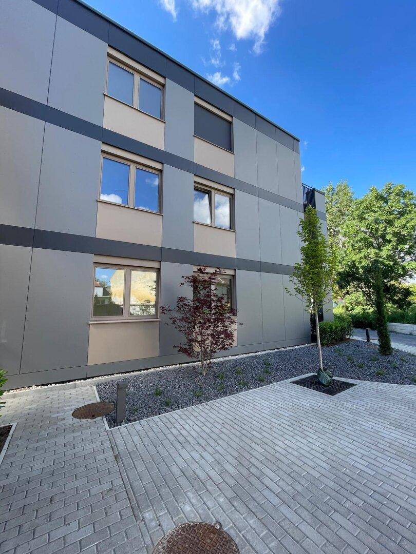 Moderne Gebäudefassade mit großen Fenstern und gepflastertem Zugangsbereich.