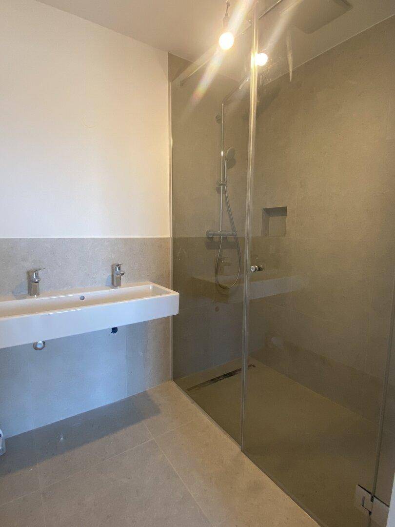 Modernes Badezimmer mit Doppelwaschbecken, großer begehbarer Dusche und hellen Fliesen.