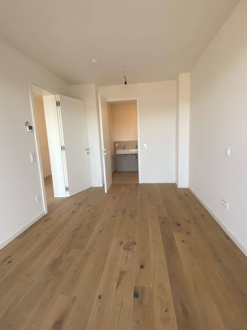 Helles Schlafzimmer mit Holzboden und Zugang zu einem angrenzenden Badezimmer.