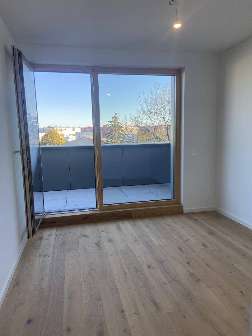 Helles Schlafzimmer mit Holzboden und großen Falttüren, die auf einen Balkon führen.