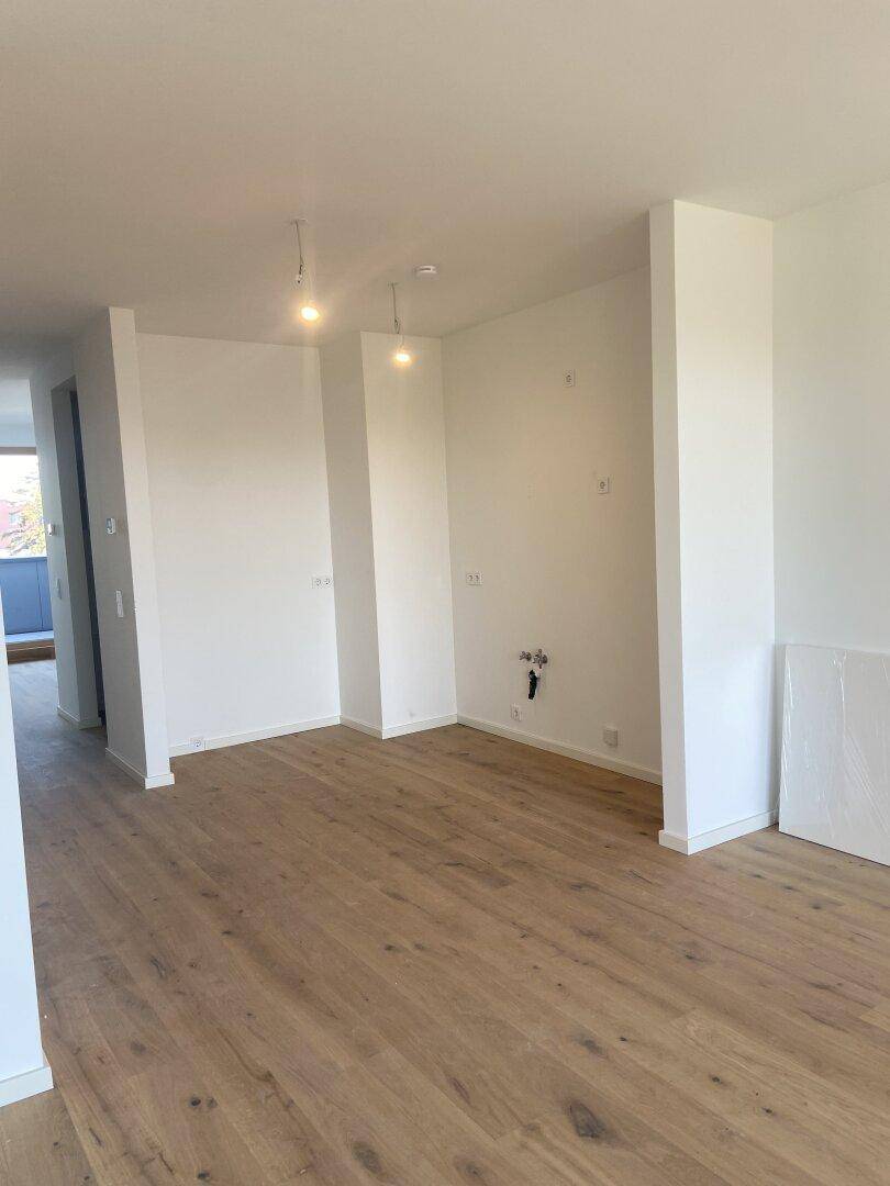 Leerer Raum mit Holzboden und weißen Wänden, vorbereitet für die Installation einer Küche.