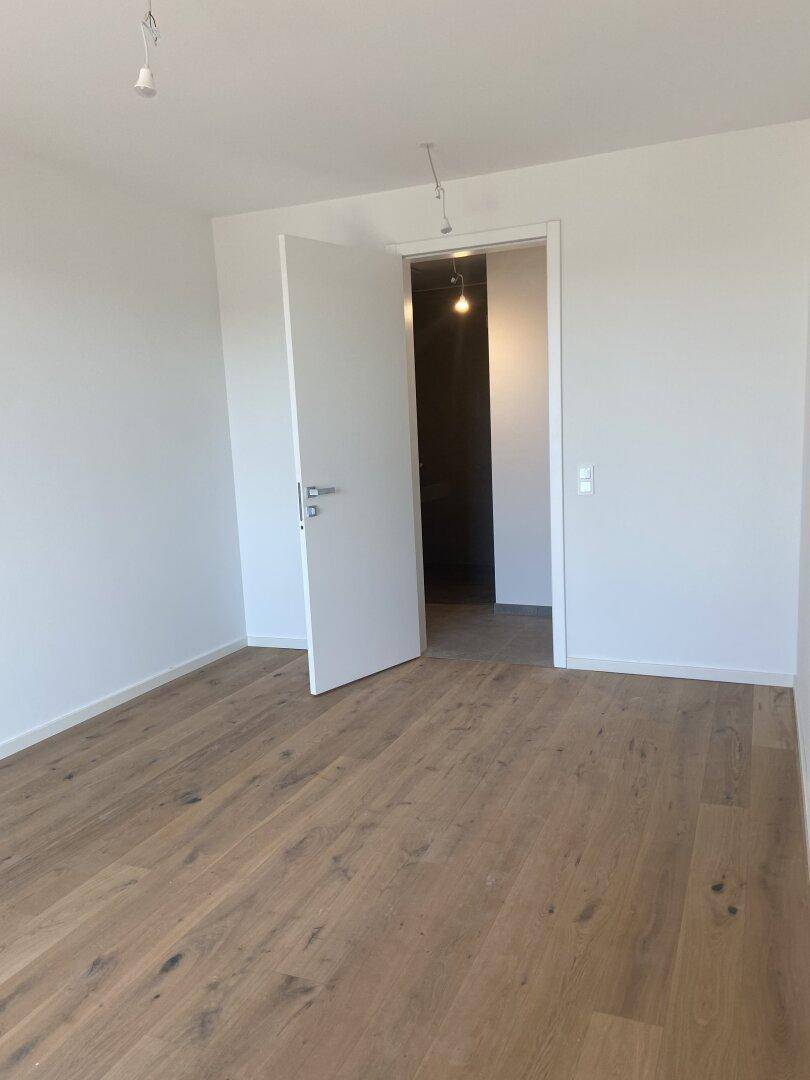 Leeres Zimmer mit Holzboden und weißen Wänden, ideal als Schlaf- oder Arbeitszimmer.