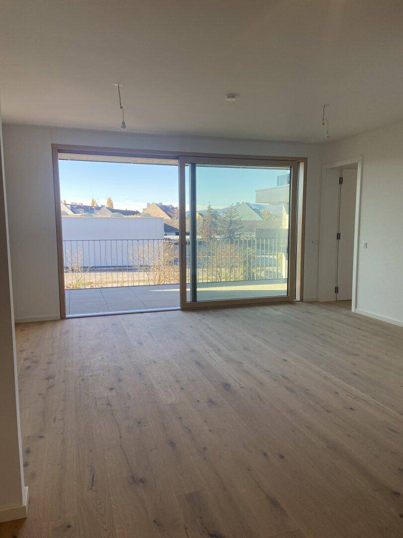 Heller Wohnraum mit Holzboden und großen Fenstern, die Zugang zu einem Balkon bieten.